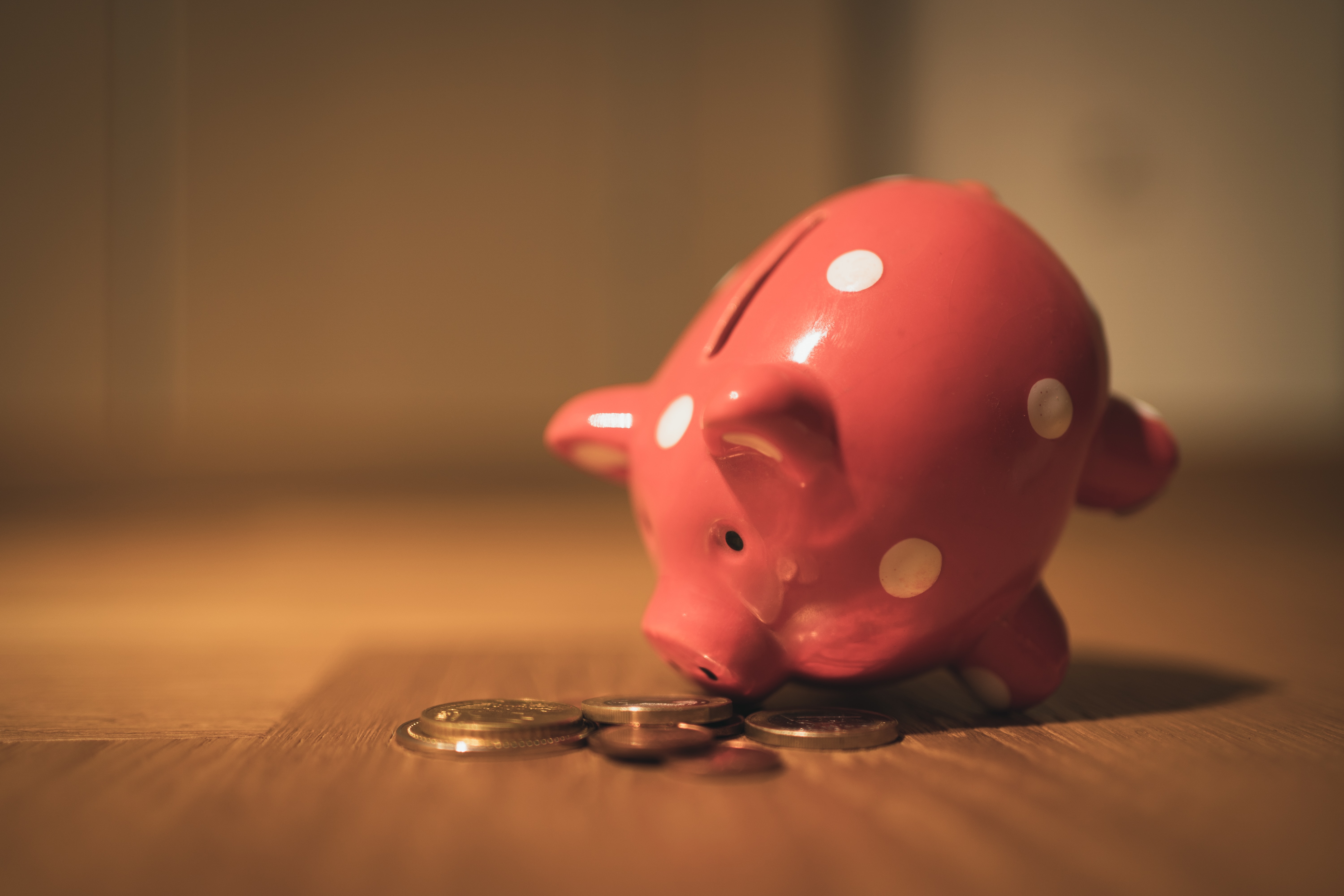 Pink piggy bank with coins on wooden floor
