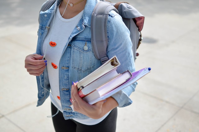 girl in jeans jacket holding books with a backpack