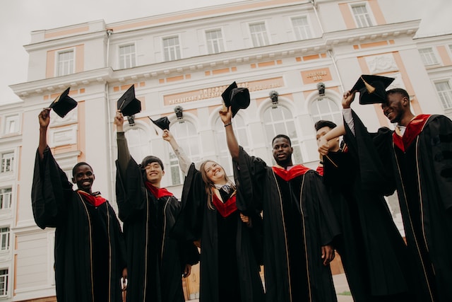 Six students throwing graduation hat in front of white building