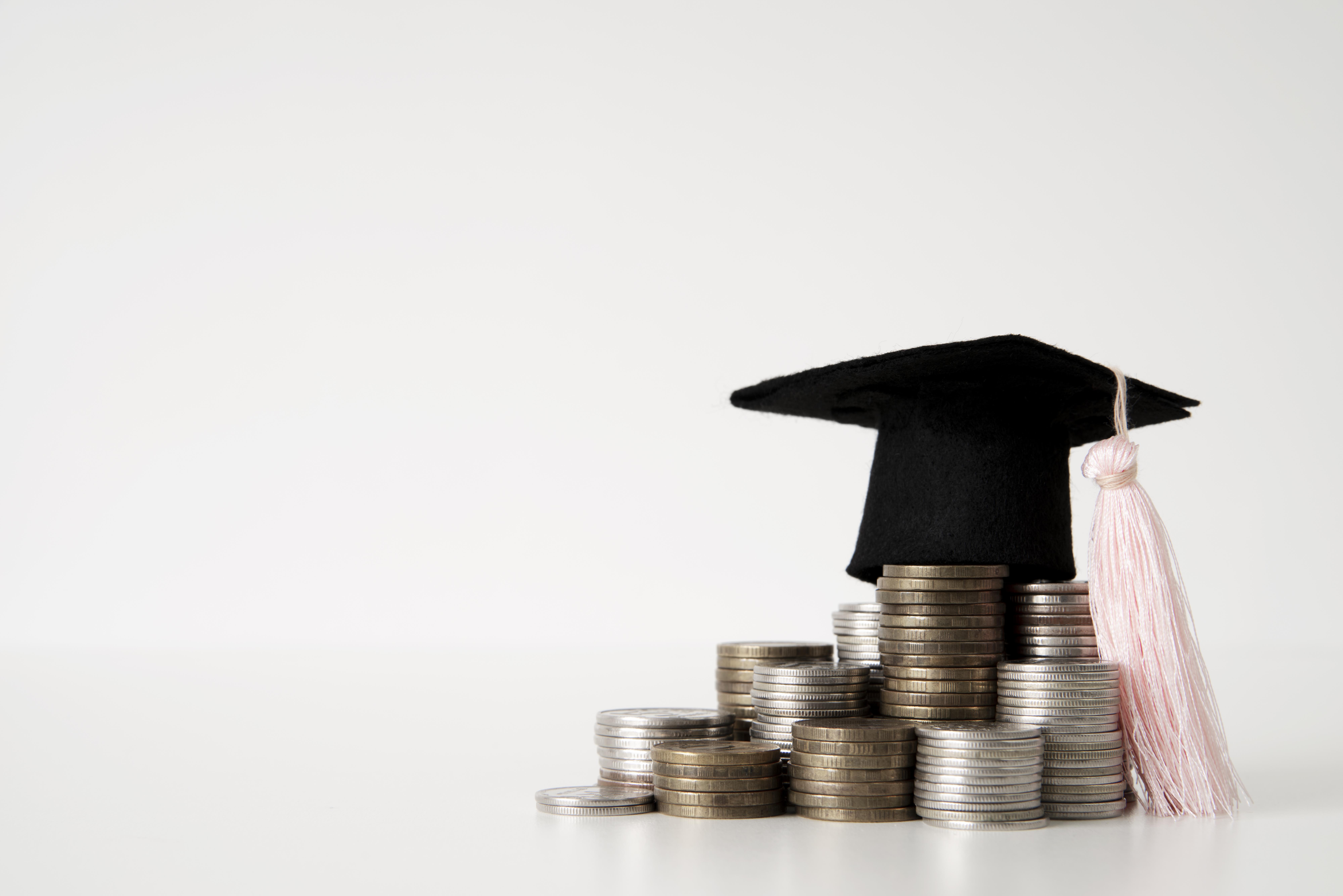 Small graduation hat on a pile of coins with white background
