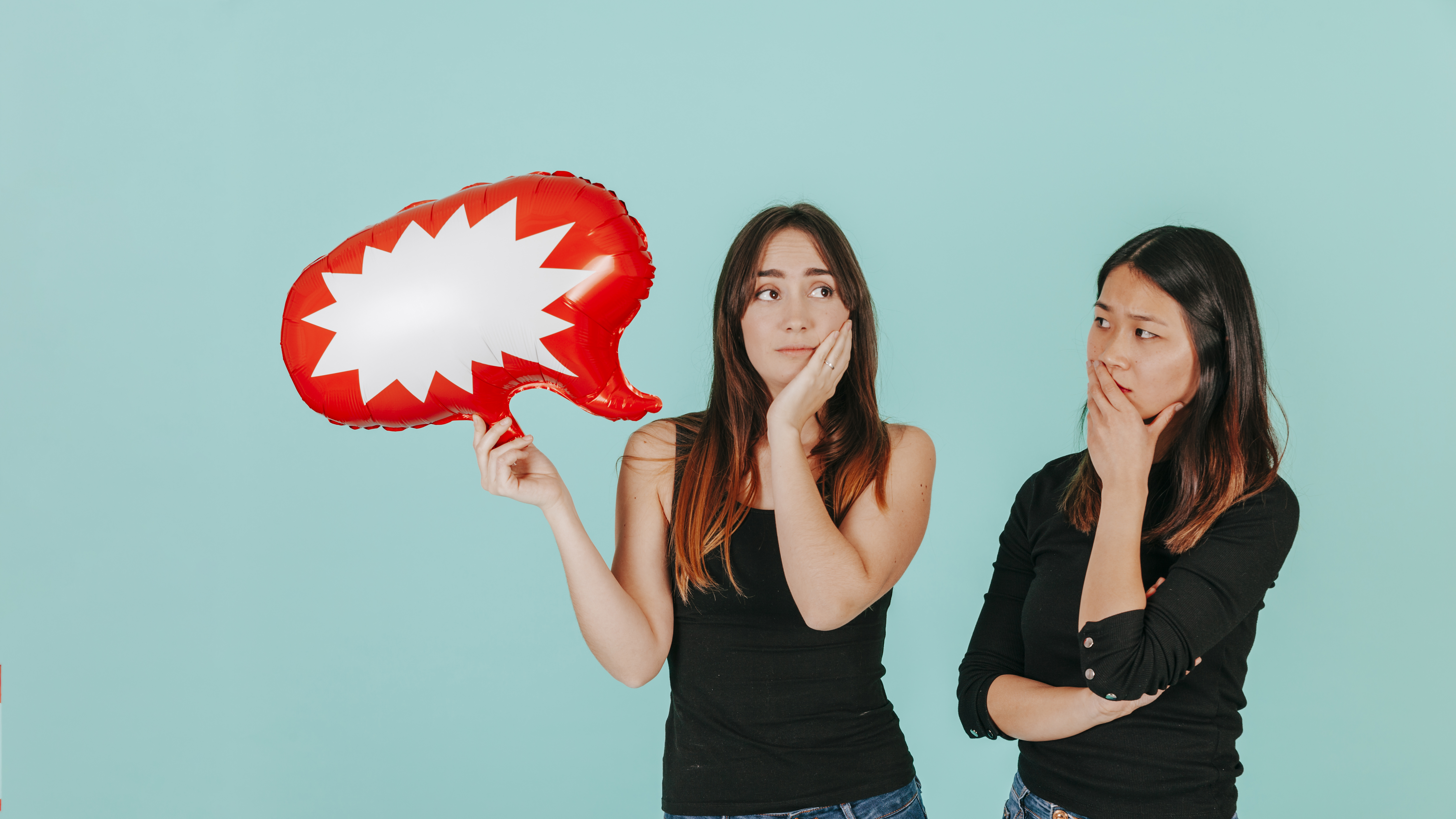 Girl holding red ballon with speech bubble and asian girl looking puzzled 