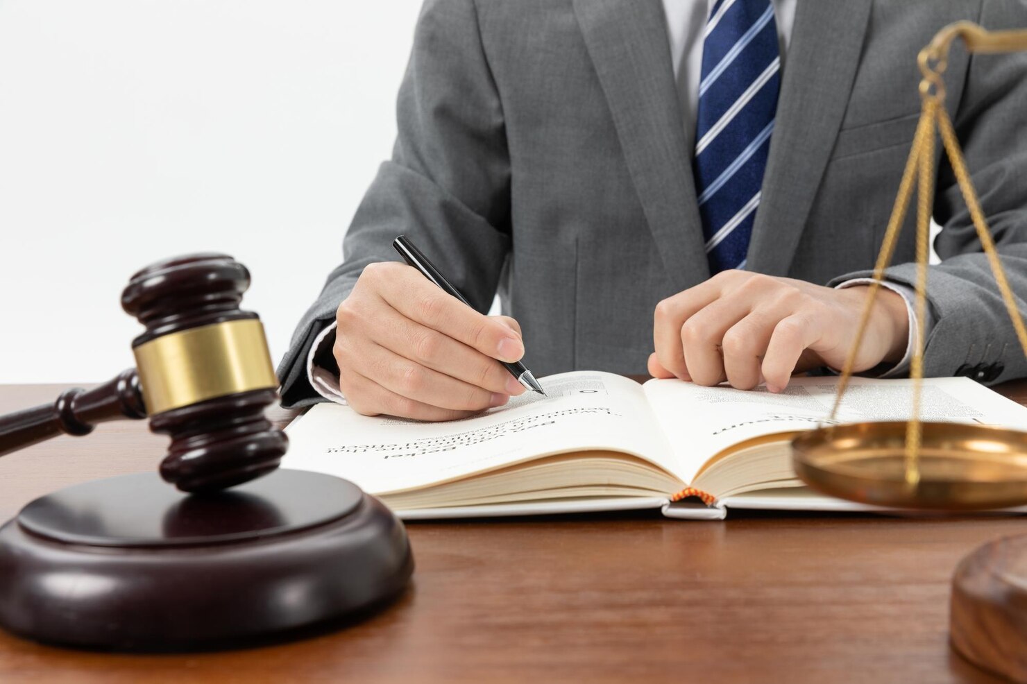 Person writing on book with gavel and balance on the table 