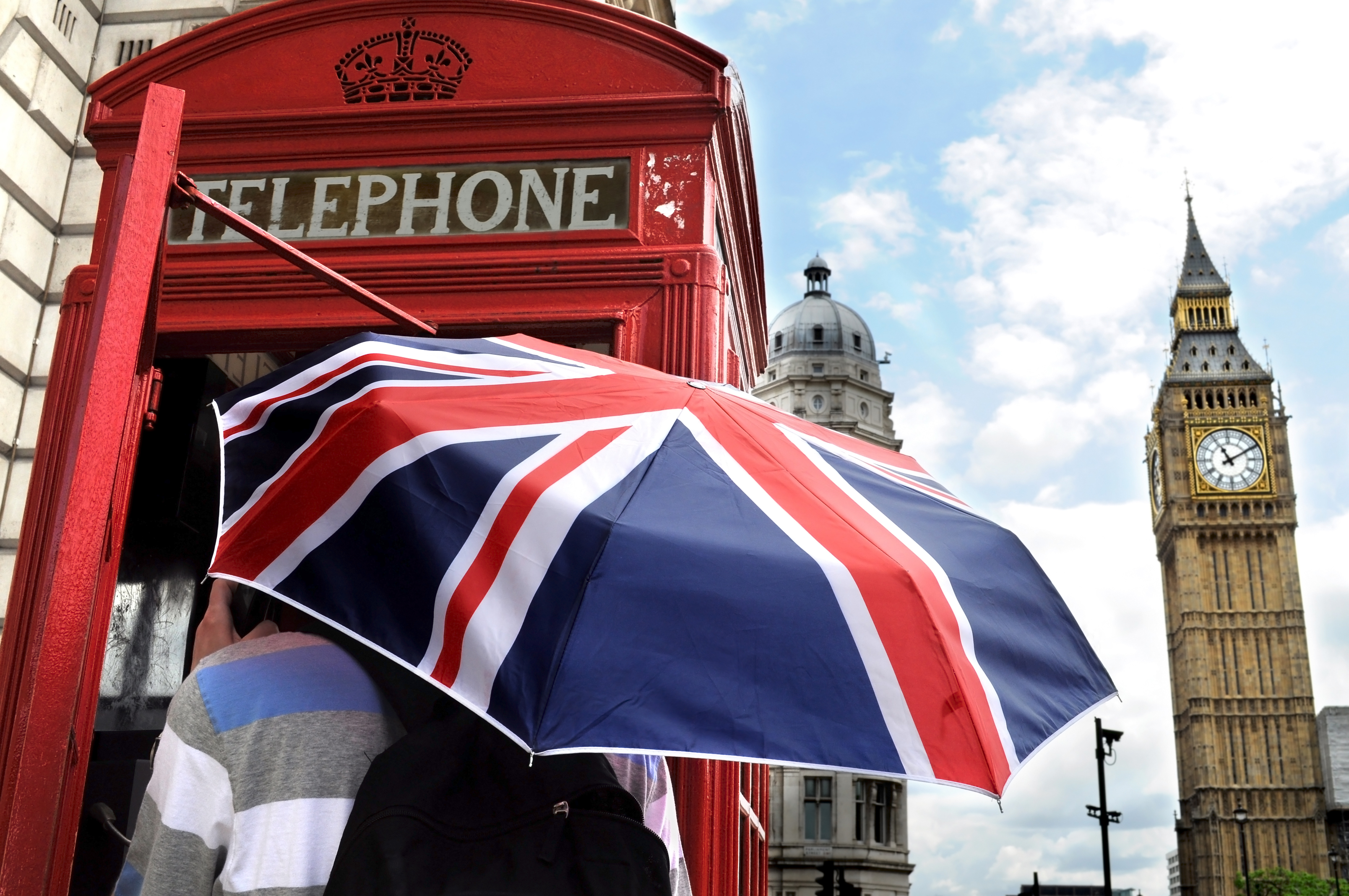 Male holding uk flag umbrella in London telephone booth next to Big Ben 